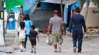Migrantes caminan entre casas de campaña