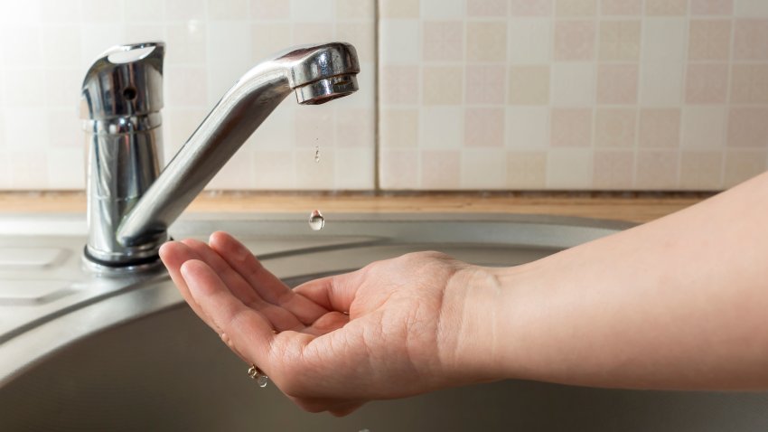 A drop of water drips from faucet in human palm above round metal kitchen sink