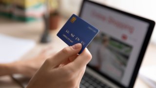 Foto de una persona con una tarjeta de crédito en la mano y una computadora portátil al frente.