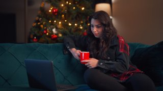 A young woman is relaxing at home and using her laptop in the living room during Christmas.