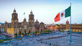 The Mexican flag flies over the Zocalo, the main square in Mexico City. The Metropolitan Cathedral faces the square, also referred to as Constitution Square.