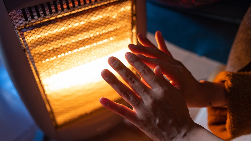 BARCELONA, SPAIN – 2022/11/20: A woman warms her hands on an electric heater at home in the Guinardo neighborhood. The increasing cost of natural gas following the Russia-Ukraine war has caused a surge of home heating prices, forcing governments in Europe and globally to provide economic support to lower incomes households. (Photo by Davide Bonaldo/SOPA Images/LightRocket via Getty Images)