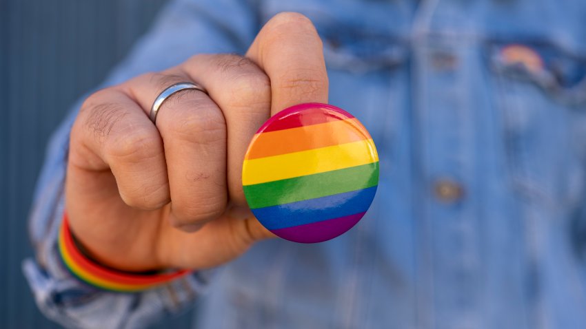 Unrecognizable man showing to the camera a rainbow LGBT pin. Pride of gays, lesbians, bisexuals and trans, respect for diversity of sexual orientation and gender identity.