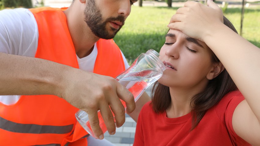 Worker with bottle of water helping woman outdoors. Suffering from heat stroke