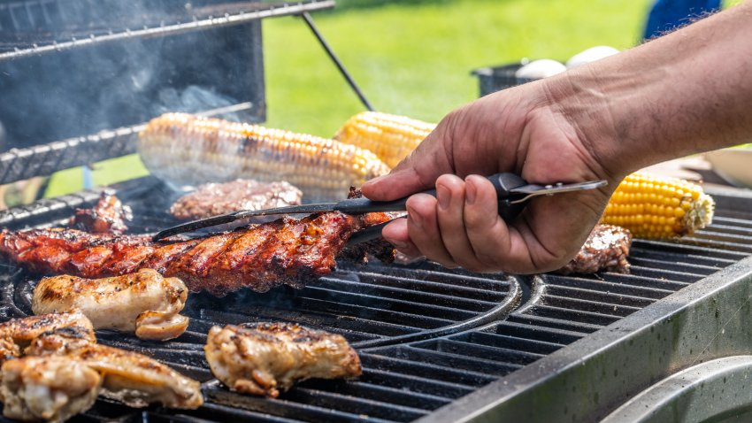 Close-up of man using tongs to take meat off on hot barbecue grill.