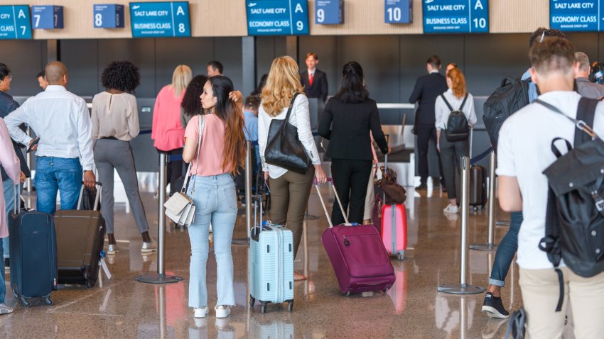 Diverse people checking in at the airport. Lining up, holding luggage and boarding passes. All wearing a protective face mask.