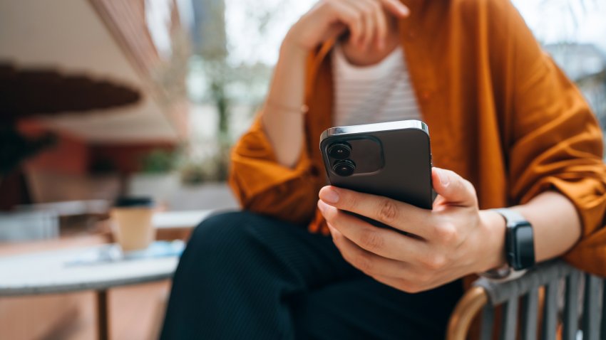 Close up shot of a young Asian woman using smartphone while sitting in an outdoor cafe and drinking coffee. Lifestyle and technology