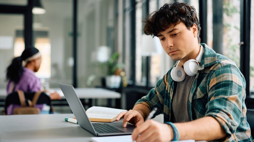 University student writing while using laptop and studying in the classroom. Copy space.