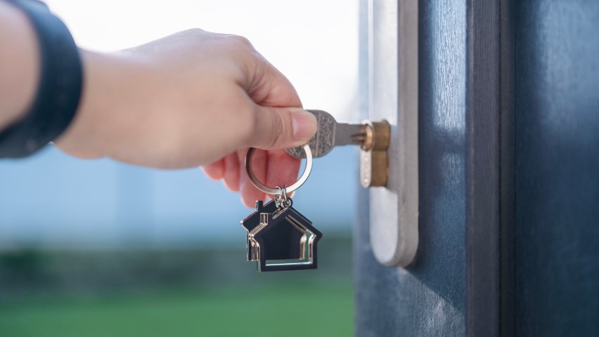 Close up of key with a keychain in the shape of a house. Open front door of house with lock. Real estate business. Renting, buying or selling a house. Mortgage concept