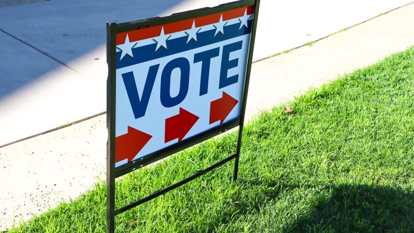 A red, white and blue sign directs citizens to the location for voting. The sign includes red directional arrows; and stars and stripes.