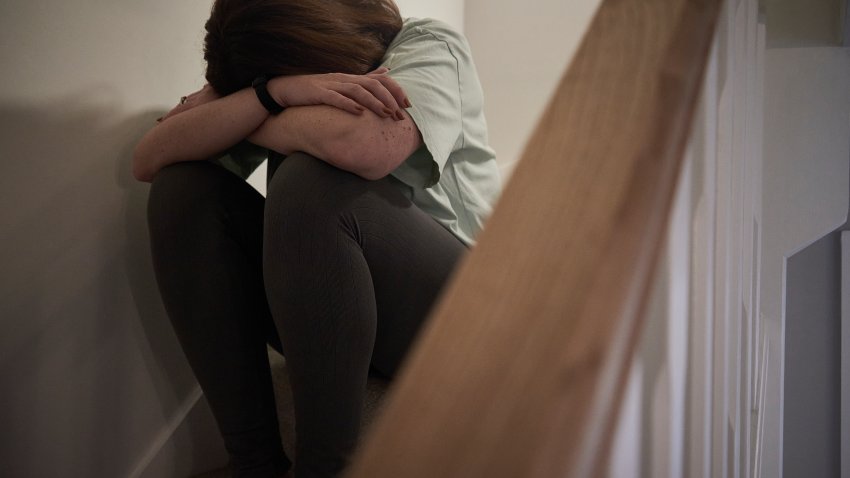 A woman suffering from depression or domestic abuse sat on the stairs of her home hiding her face.