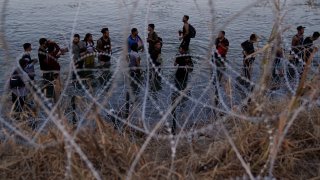 ARCHIVO - Migrantes esperan junto a una barrera de alambre de púas tras haber cruzado el rio Bravo (o Grande) desde el lado mexicano hacia Estados Unidos en Eagle Pass, Texas, el 23 de septiembre de 2023.