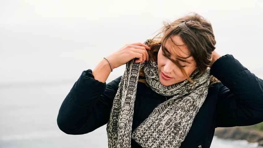 young woman rearranging here scarf while at the Cornish Coast on a September day.