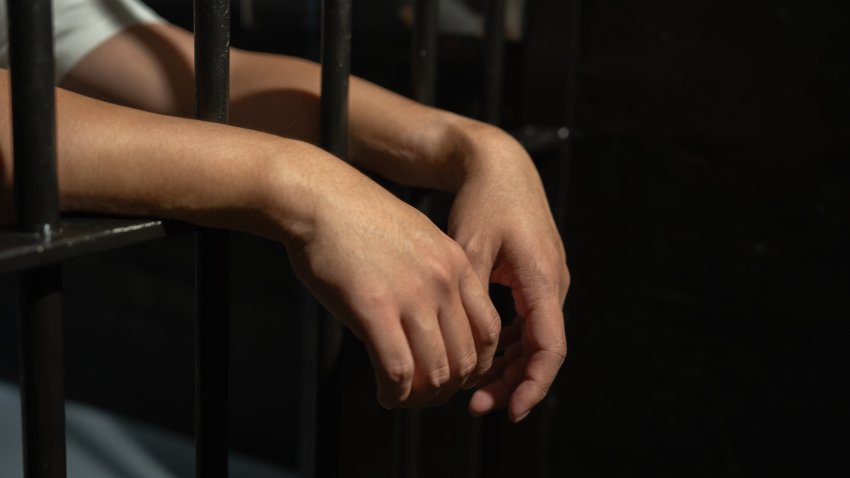 Hands of a prisoner in a cell behind bars.