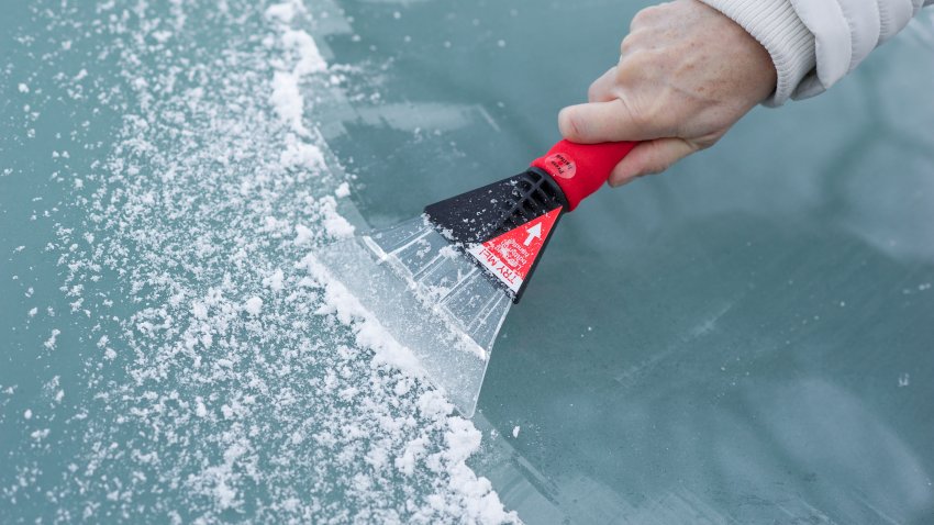 Person is scraping snow and ice from the car windscreen