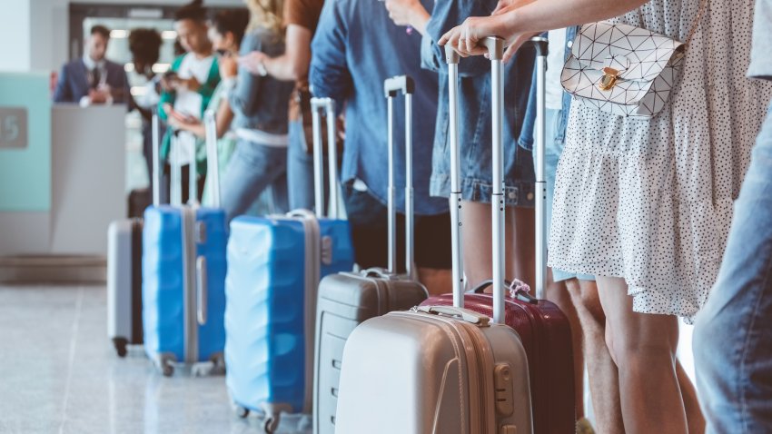 Travelers with luggage using smart phones while waiting in line for boarding at airport. Focus on wheeled luggage.