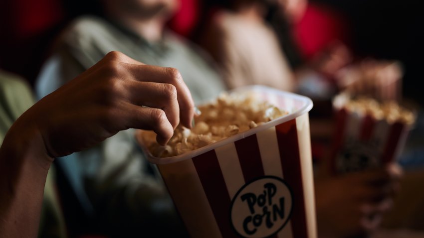 Close up of unrecognizable woman eating popcorn during movie projection in cinema.