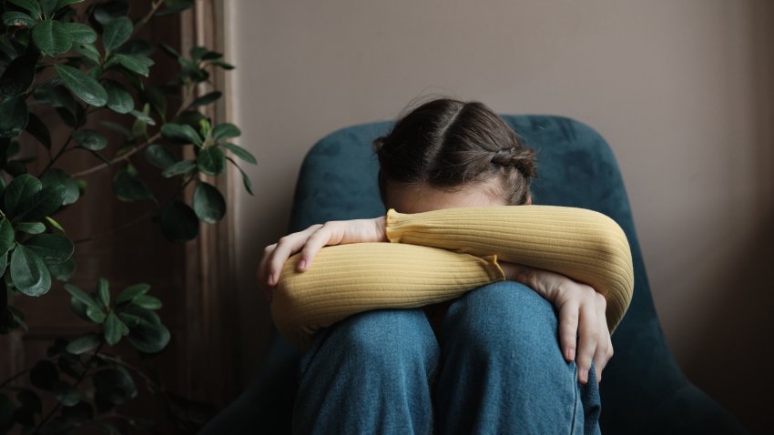 Upset depressed teenager crying at home, sad frustrated teen girl sitting by window with head on knees. Teenagers and mental health concept